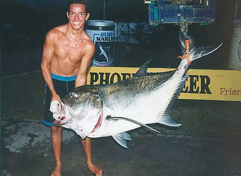 Dominique adolescent, tenant fièrement un grand poisson devant une banderole