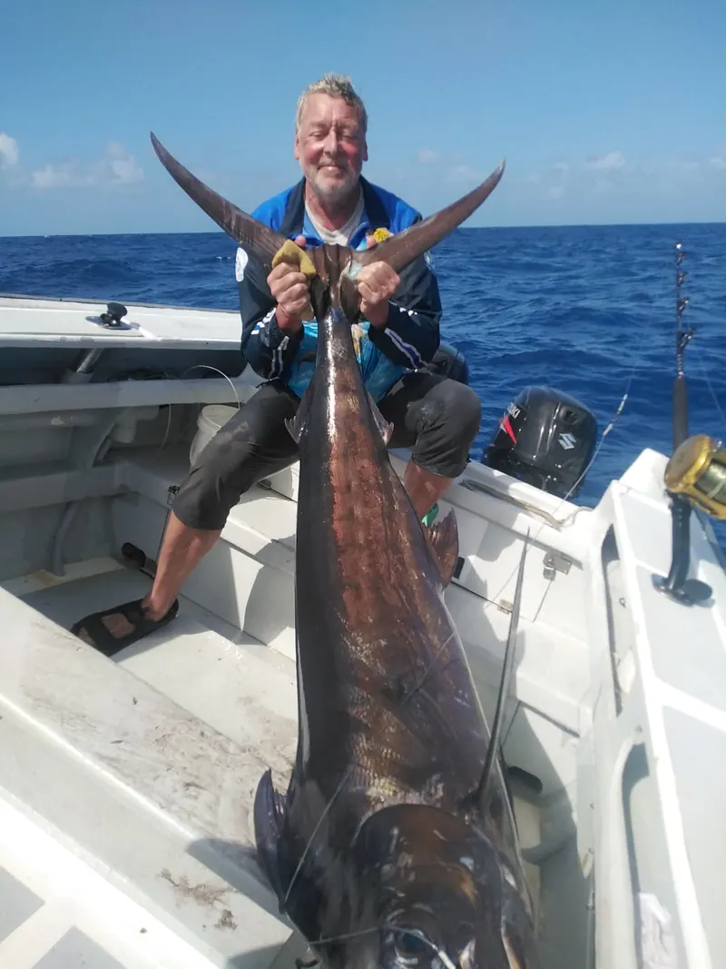 Un pêcheur tient la queue d’un marlin à l’arrière de FreeDom, en plein océan